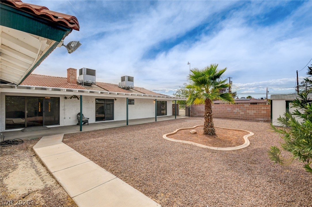 Backyard with a covered patio, gravel landscaping, and a palm tree in a curved planter.