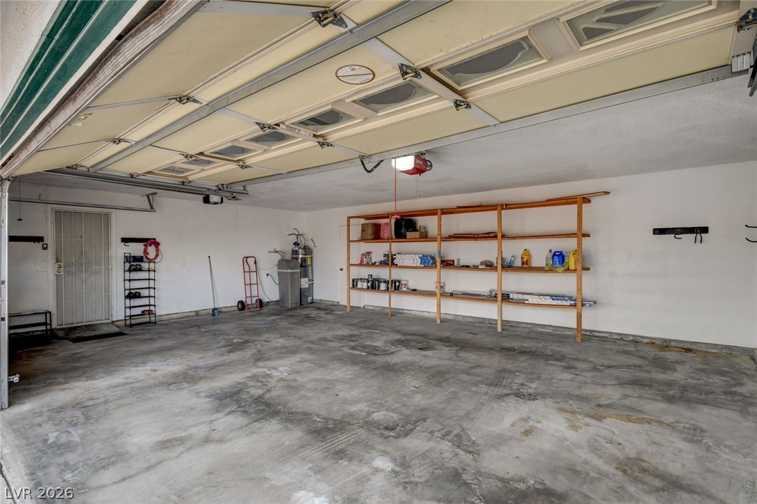 Garage with a raised door, concrete floor, and wooden storage shelves along the back wall.
