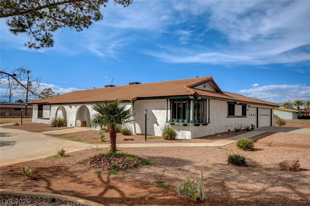 Single-story stucco home with a tile roof, arched entry, attached garage, and desert landscaping.
