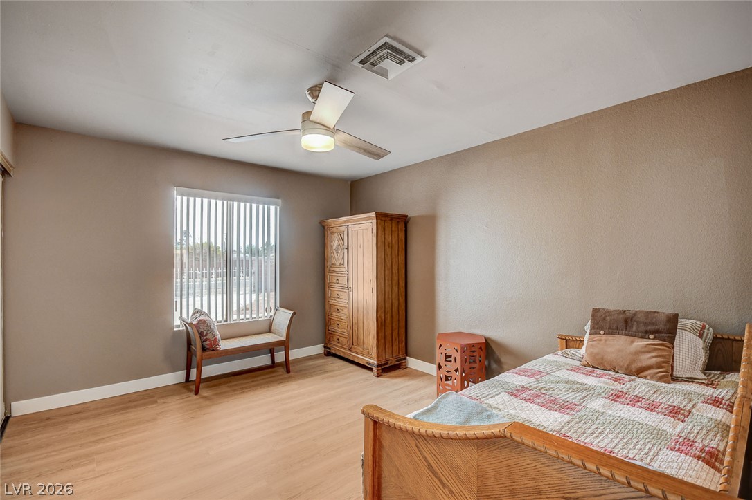 Furnished bedroom with a wooden bed, tall armoire, and bench beside a window with vertical blinds.