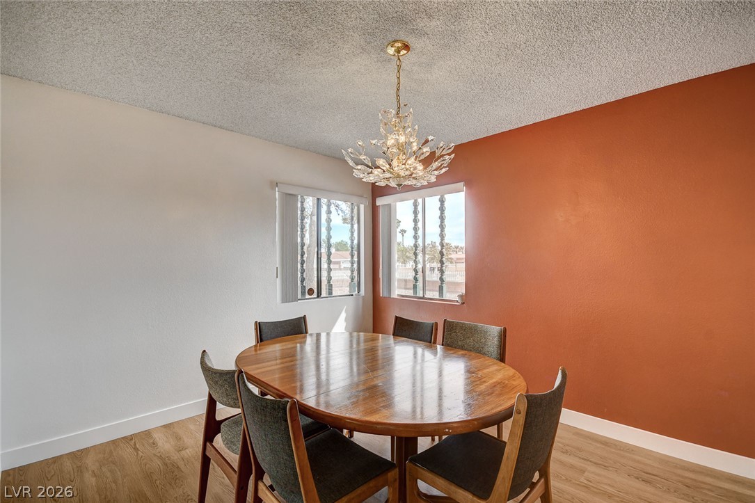 Dining room with an oval wooden table, chandelier, corner windows, and rust-colored accent wall.