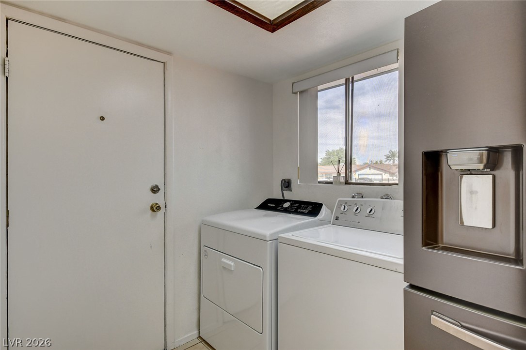 Laundry room with a washer and dryer beneath a window and a stainless steel refrigerator.
