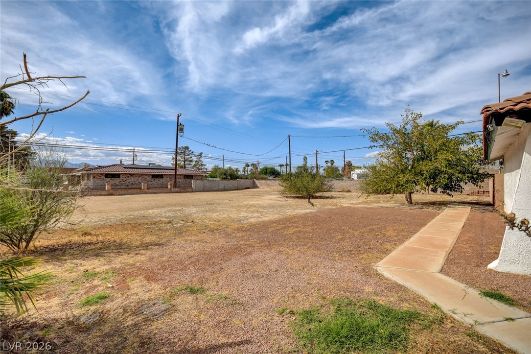 Spacious dry backyard with a concrete walkway, sparse trees, and neighboring homes.