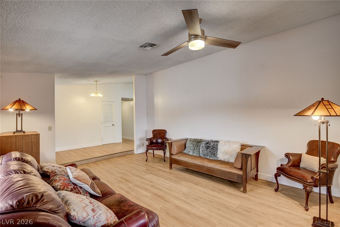 Living room with light wood flooring, leather seating, a ceiling fan, and a raised adjoining area.