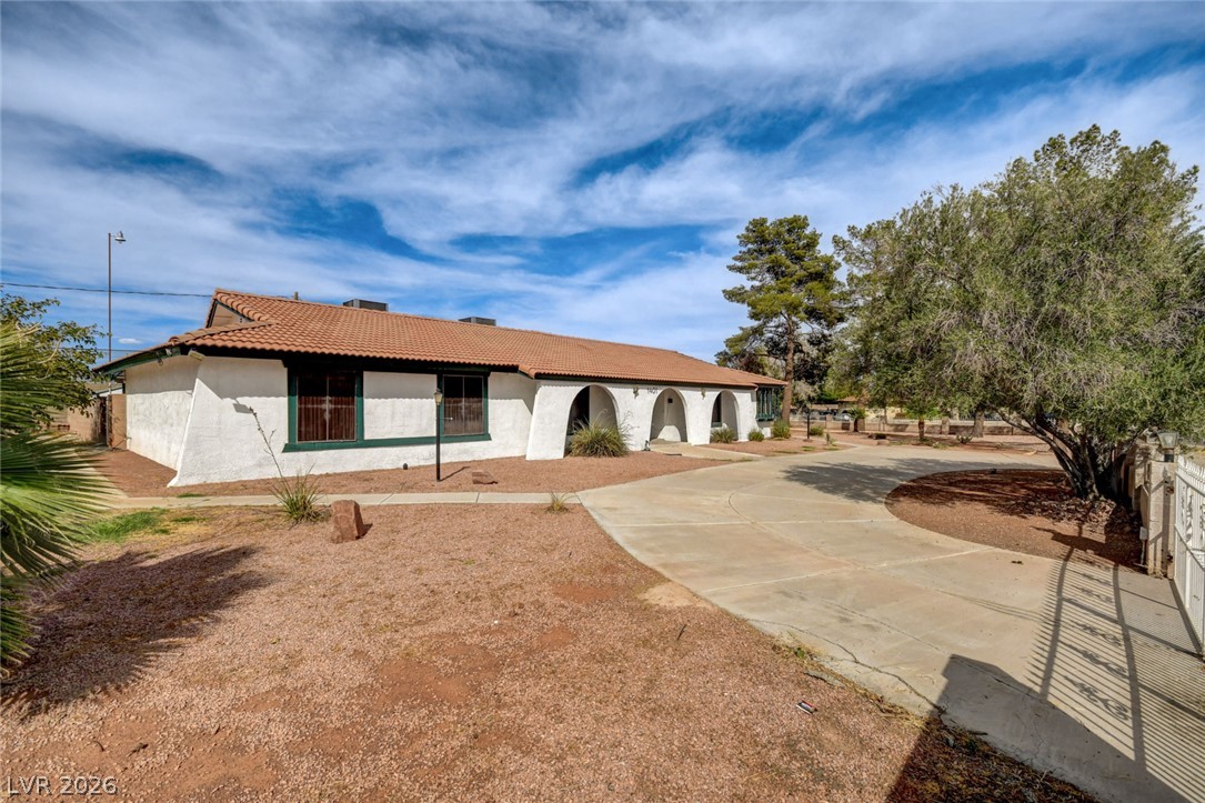 Single-story stucco home with terracotta tile roof, arched entry, gravel yard, and curved driveway.