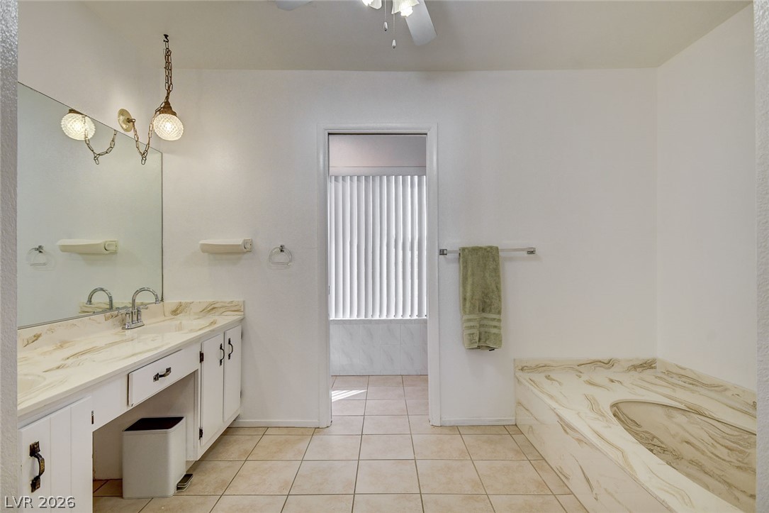 Bathroom with a long white vanity, large mirror, and raised marble-look tub surround.