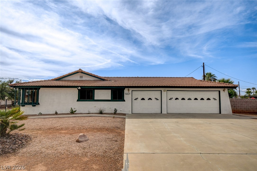 Single-story house with green trim, a two-car garage, and a gravel desert yard.