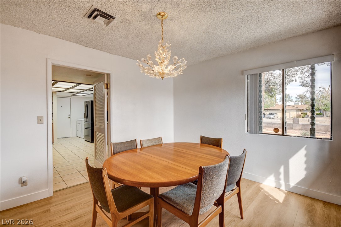 Dining room with an oval wooden table, upholstered chairs, and a branching crystal chandelier.