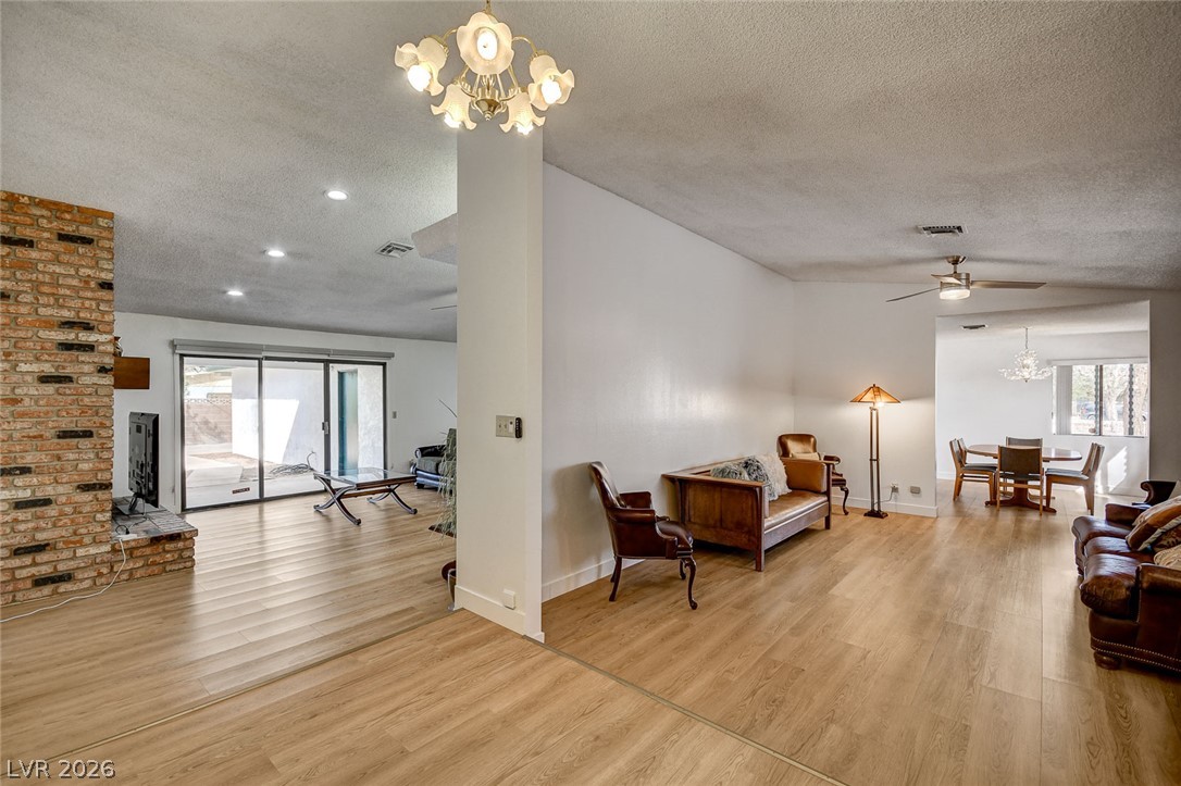 Open-plan living room with a brick fireplace, light wood floors, and sliding glass doors.
