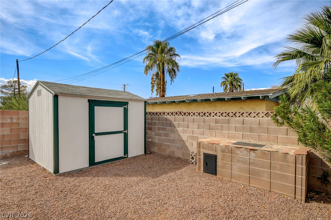 Gravel backyard with a white storage shed and low block enclosure.