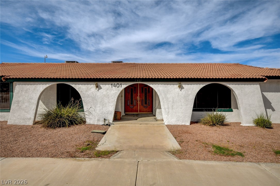 Single-story stucco house with arched openings, a terracotta tile roof, and ornate red double doors.