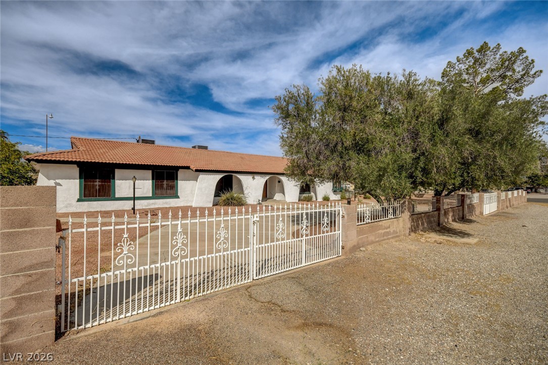Single-story stucco home with a tile roof, arched entryways, decorative gate, and large shade tree.