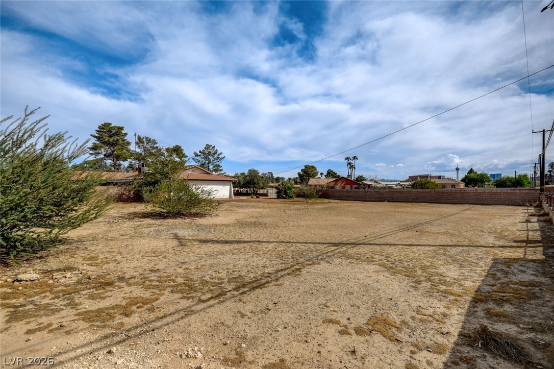 Mostly bare dirt lot with sparse shrubs and a block wall at the rear.