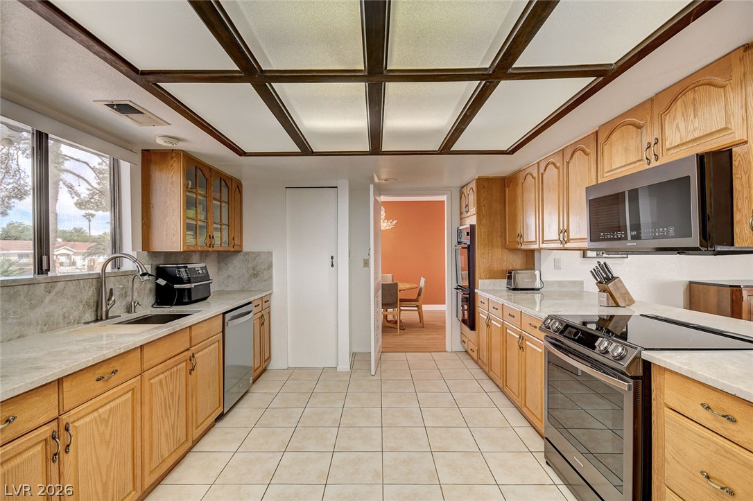 Kitchen with wood cabinetry, stainless steel appliances, and dark wood ceiling beams.