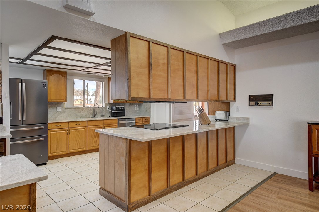Kitchen with honey-colored wood cabinets, a large stone-topped peninsula, and stainless steel appliances.