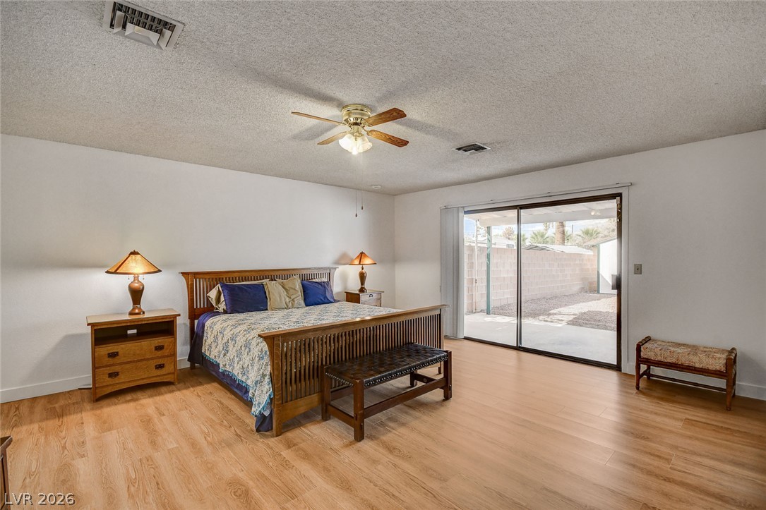 Furnished bedroom with a wooden bed, ceiling fan, and sliding glass door to a walled backyard.