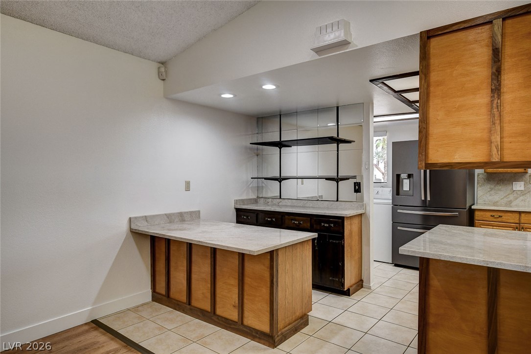Kitchen with a wood-paneled island, stone countertops, open shelving, and stainless-steel refrigerator.