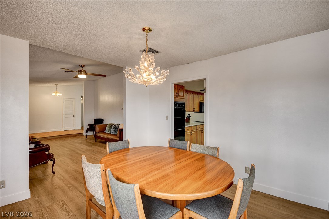 Dining area with an oval wood table, gray chairs, and a crystal chandelier beside the living room.