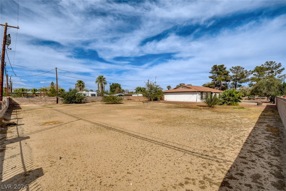 Broad dry lot enclosed by block walls, with a stucco building and palm trees in the distance.