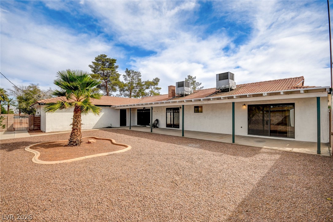 Rear exterior of a single-story home with a covered patio and gravel yard.
