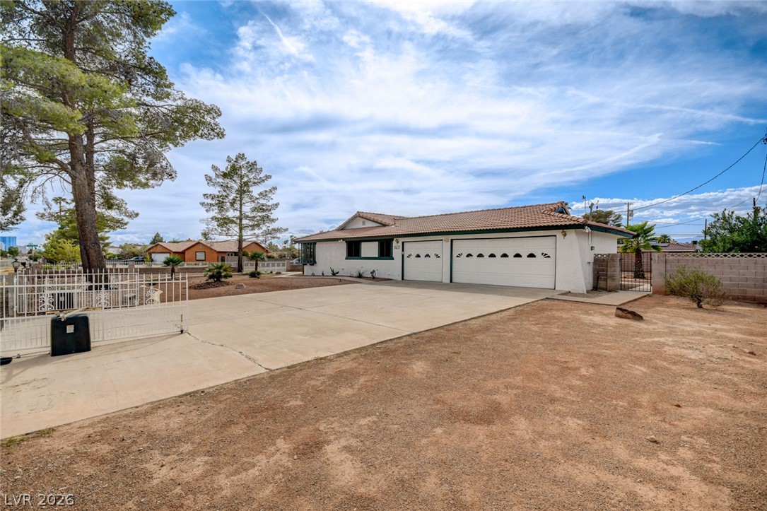 Single-story stucco home with two garage doors, a wide concrete driveway, and a dry front yard.