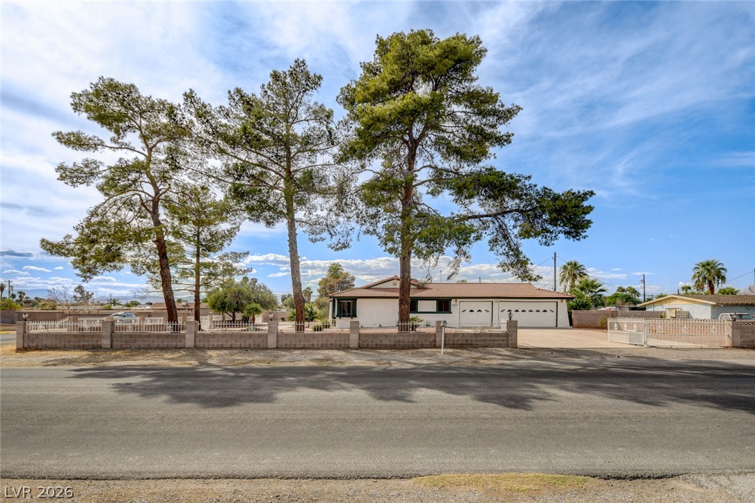 Single-story home behind a low block wall, framed by tall pine trees.