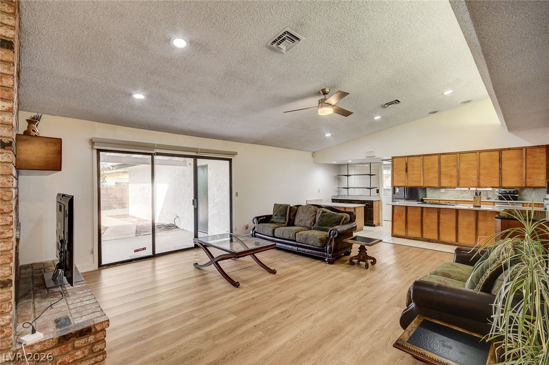 Living room opening to a kitchen, with a brick fireplace and sliding glass doors to the patio.
