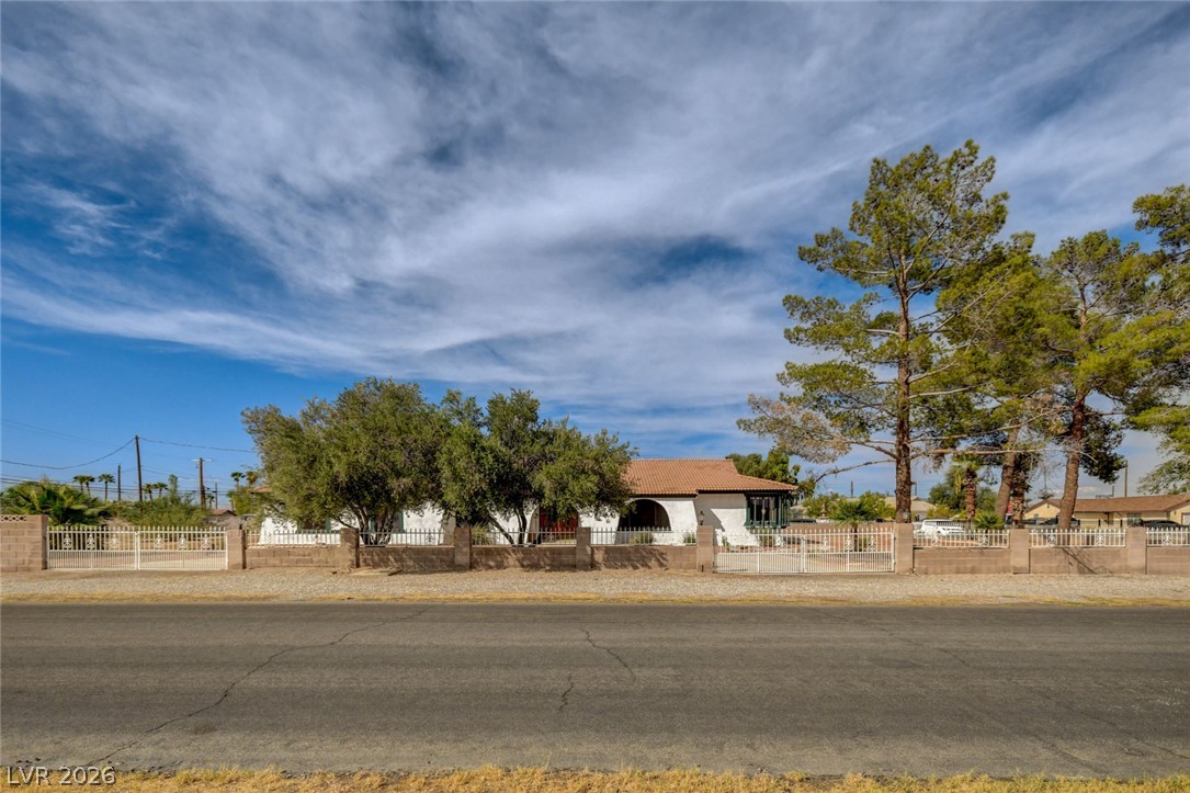 Single-story home with a tiled roof, mature trees, and a metal fence along the street.