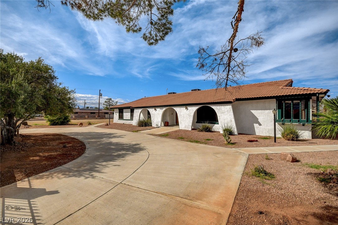 Single-story stucco home with arched openings, a tile roof, and a curved driveway.