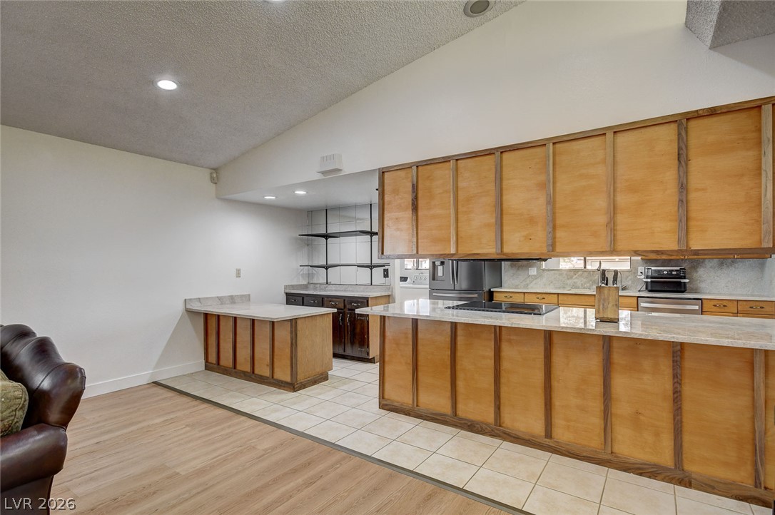 Kitchen with honey-colored wood cabinets, a large stone-counter peninsula, and stainless steel appliances.
