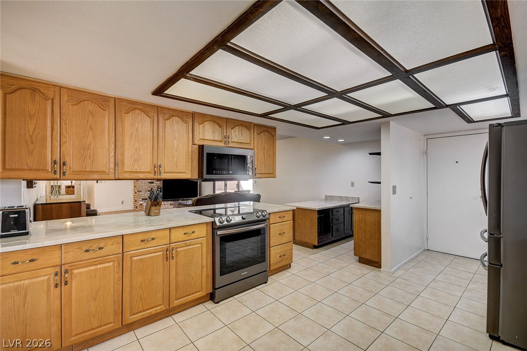 Kitchen with honey-colored cabinets, stone counters, stainless steel appliances, and a dark wood grid ceiling.