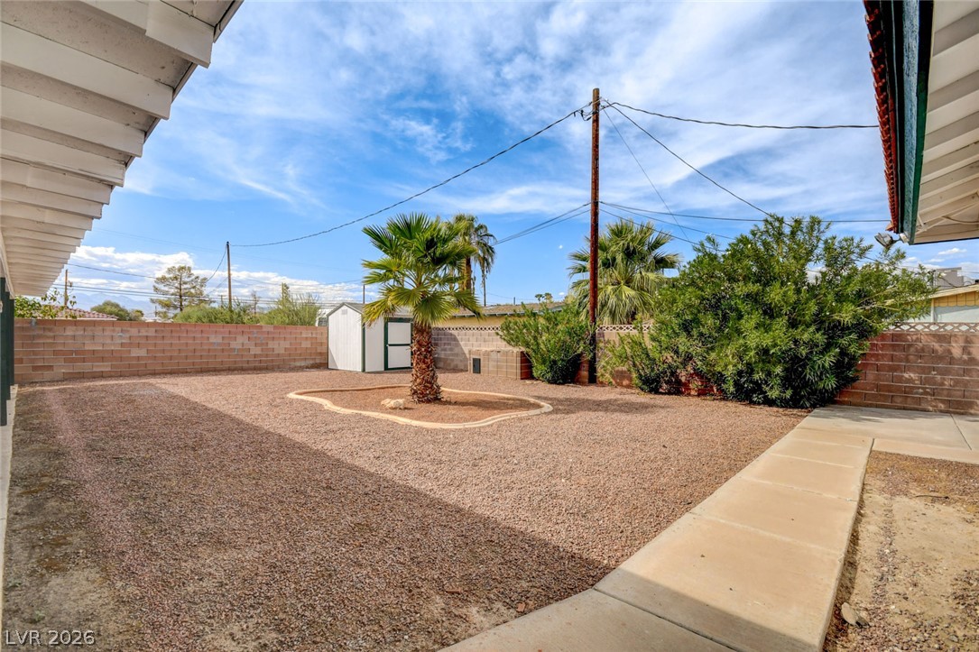 Gravel backyard with a small palm, storage shed, block walls, and a concrete walkway.