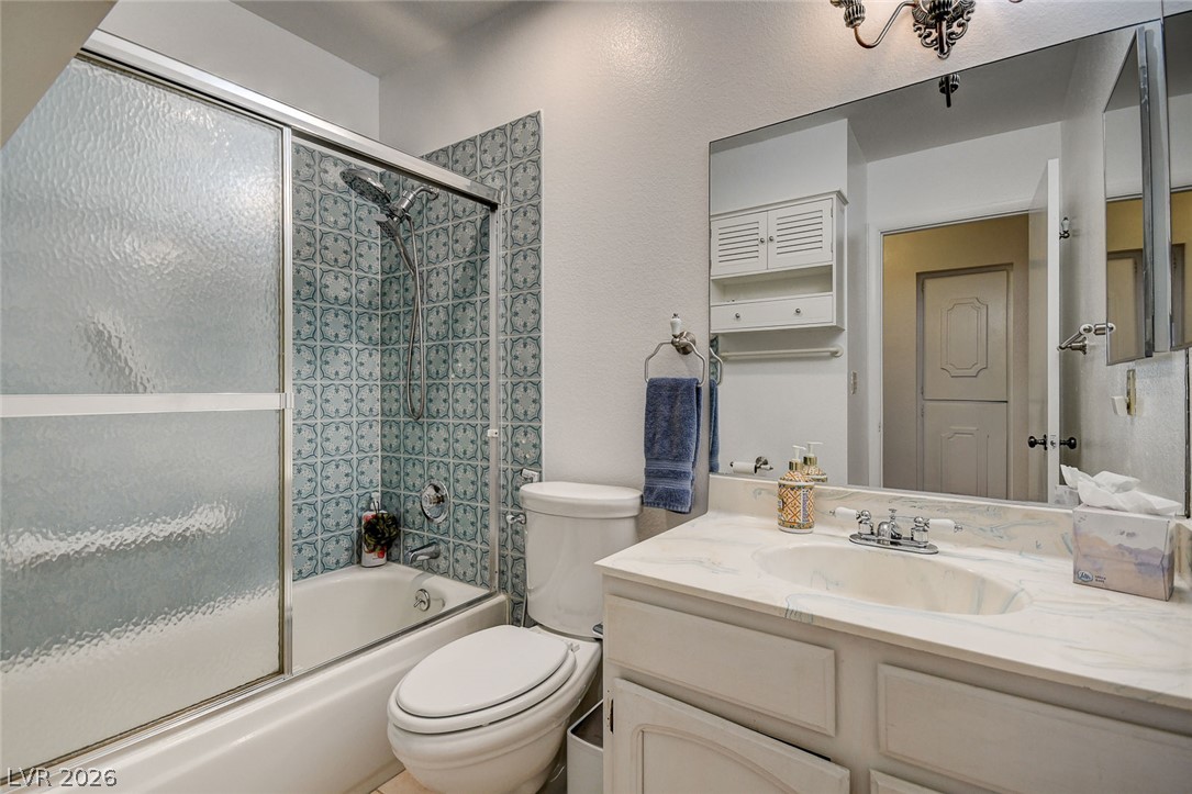 Bathroom with a tub-shower featuring patterned tile and frosted-glass doors, beside a white vanity.
