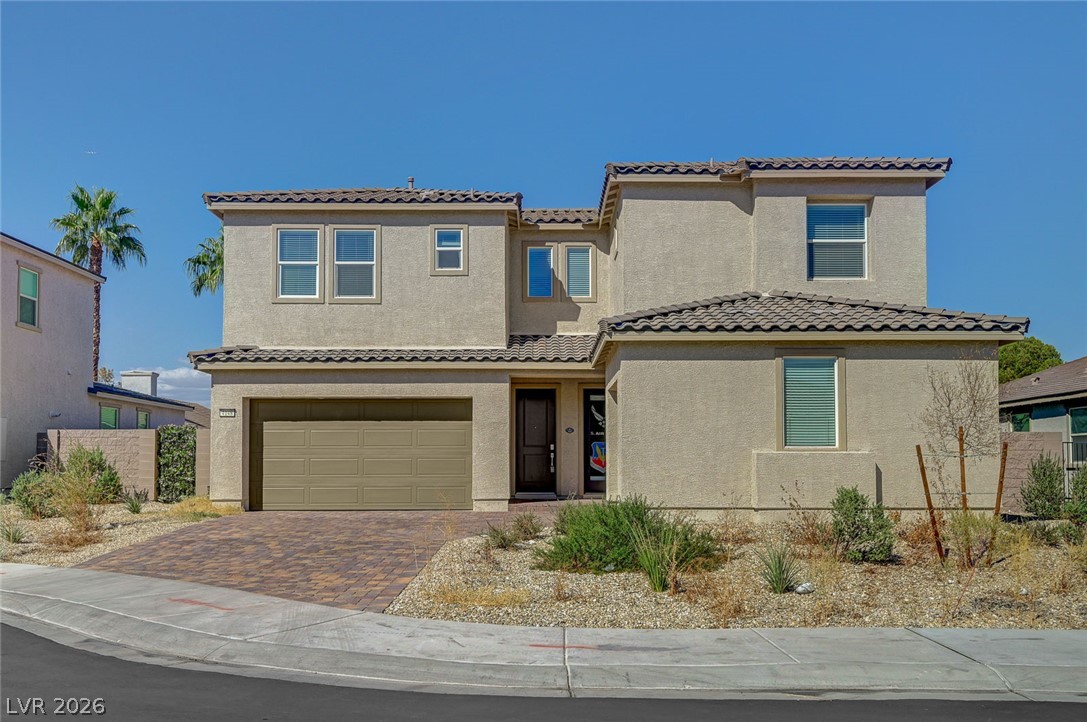 Two-story stucco house with an attached garage, paver driveway, and desert landscaping.