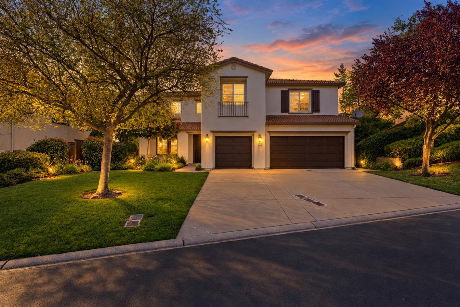 Two-story home with a two-car garage, landscaped lawn, and broad driveway at dusk.