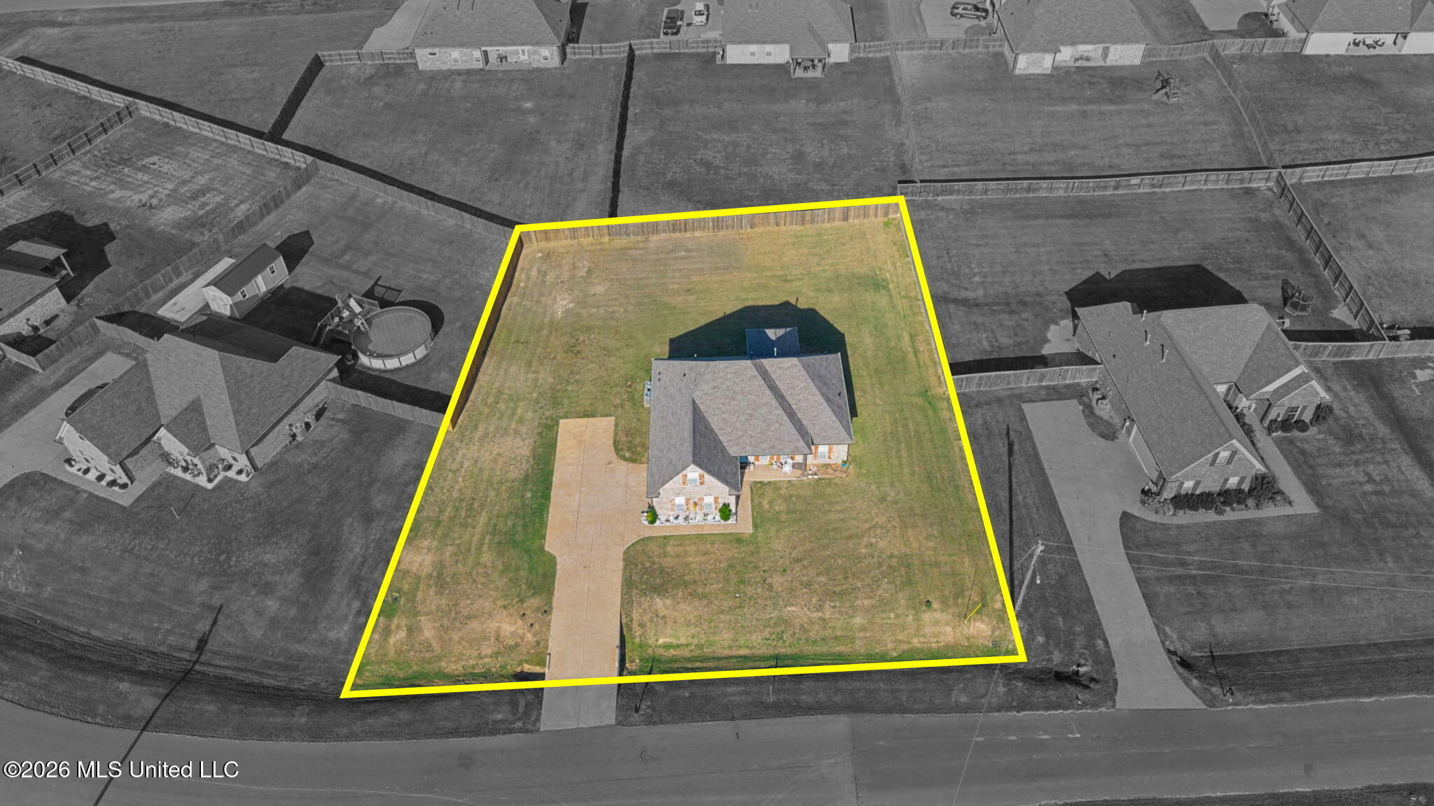 Aerial view of a house on a large fenced lot, outlined in yellow, with a long driveway.