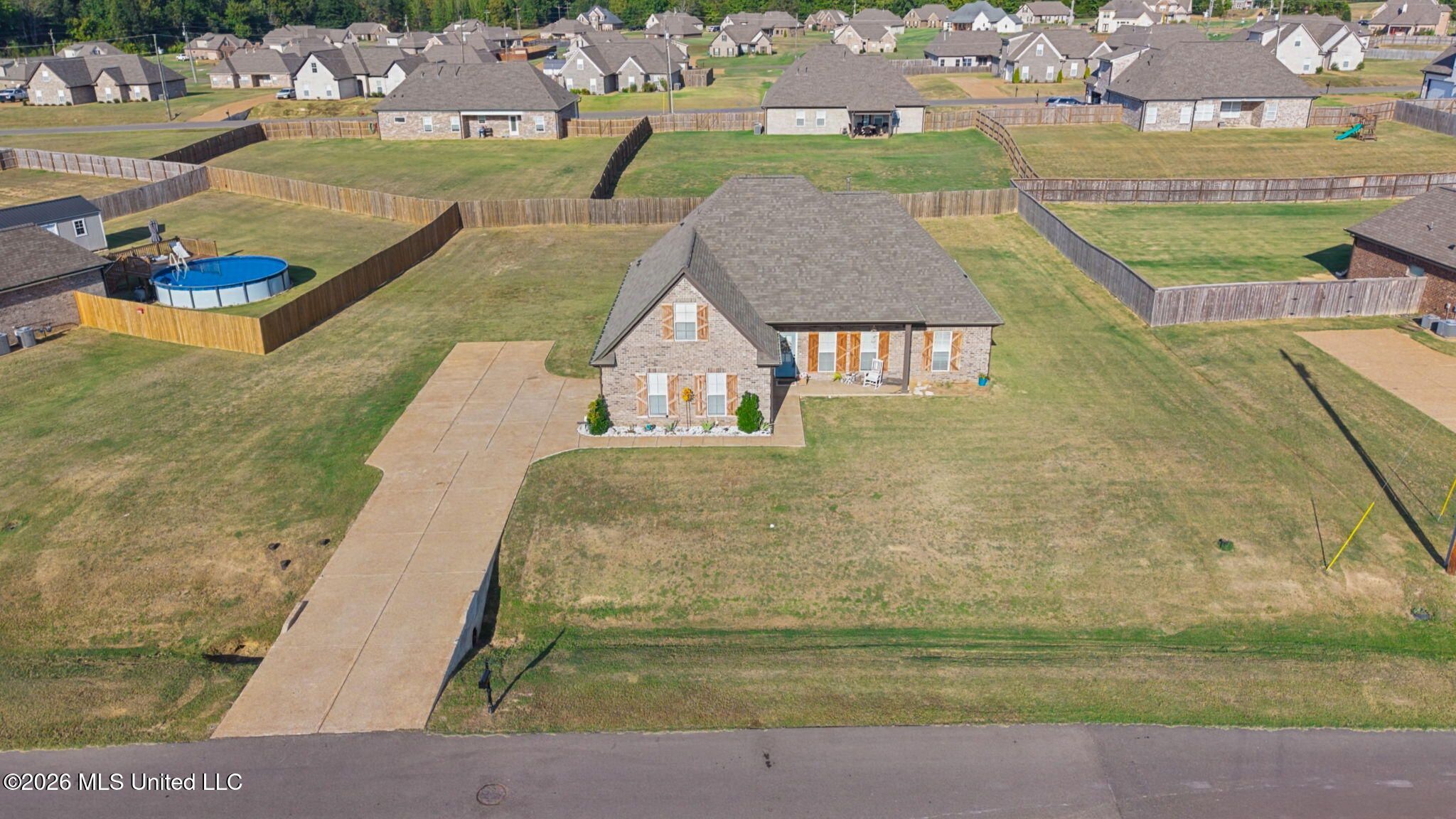 Aerial view of a brick home with a large fenced yard and concrete driveway.