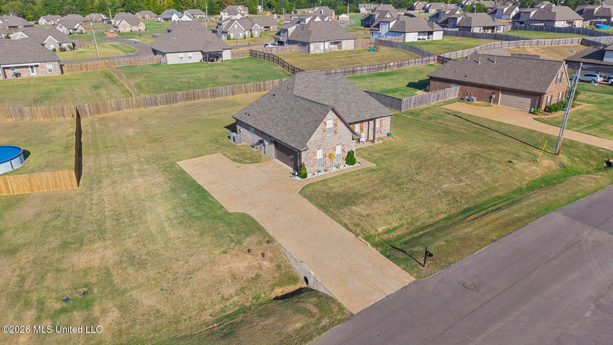 Aerial view of a brick home with a broad fenced yard and concrete driveway.