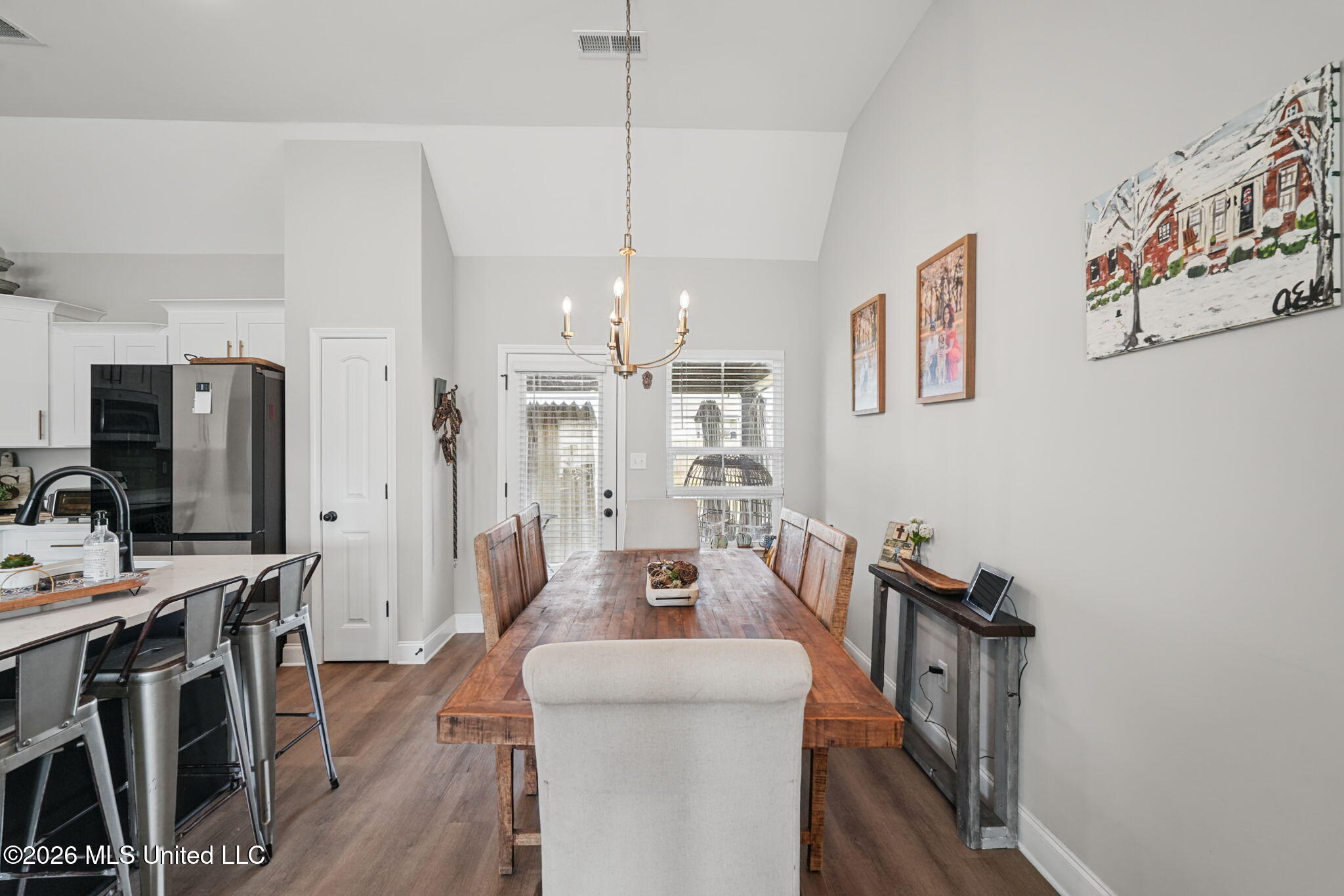 Dining area with a rustic wooden table, brass chandelier, and open white kitchen.