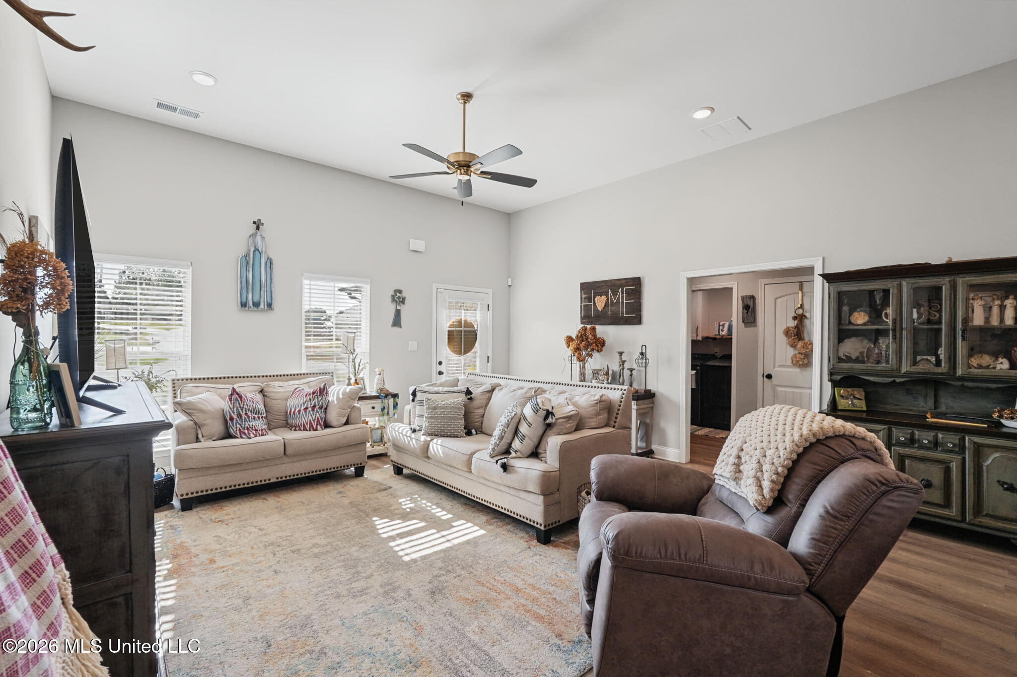 Living room with two light sofas, a brown recliner, and a ceiling fan beneath a high ceiling.