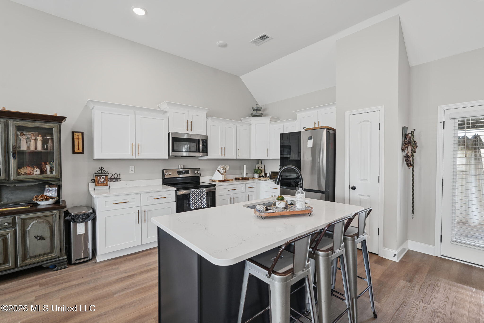 Kitchen with a large quartz island, white cabinets, stainless steel appliances, and a vaulted ceiling.