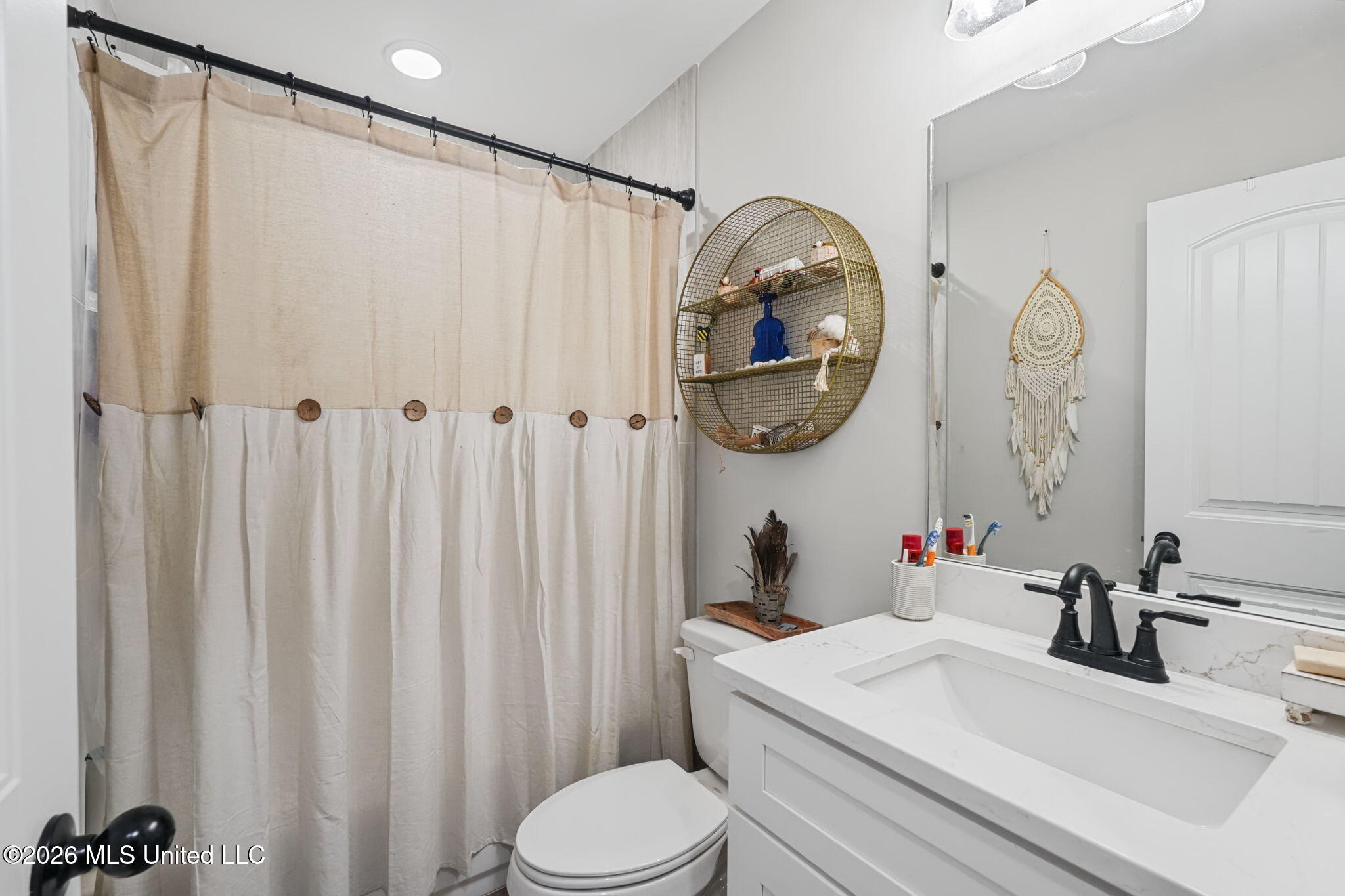 Bathroom with white vanity, black faucet, beige shower curtain, and round wire wall shelf.