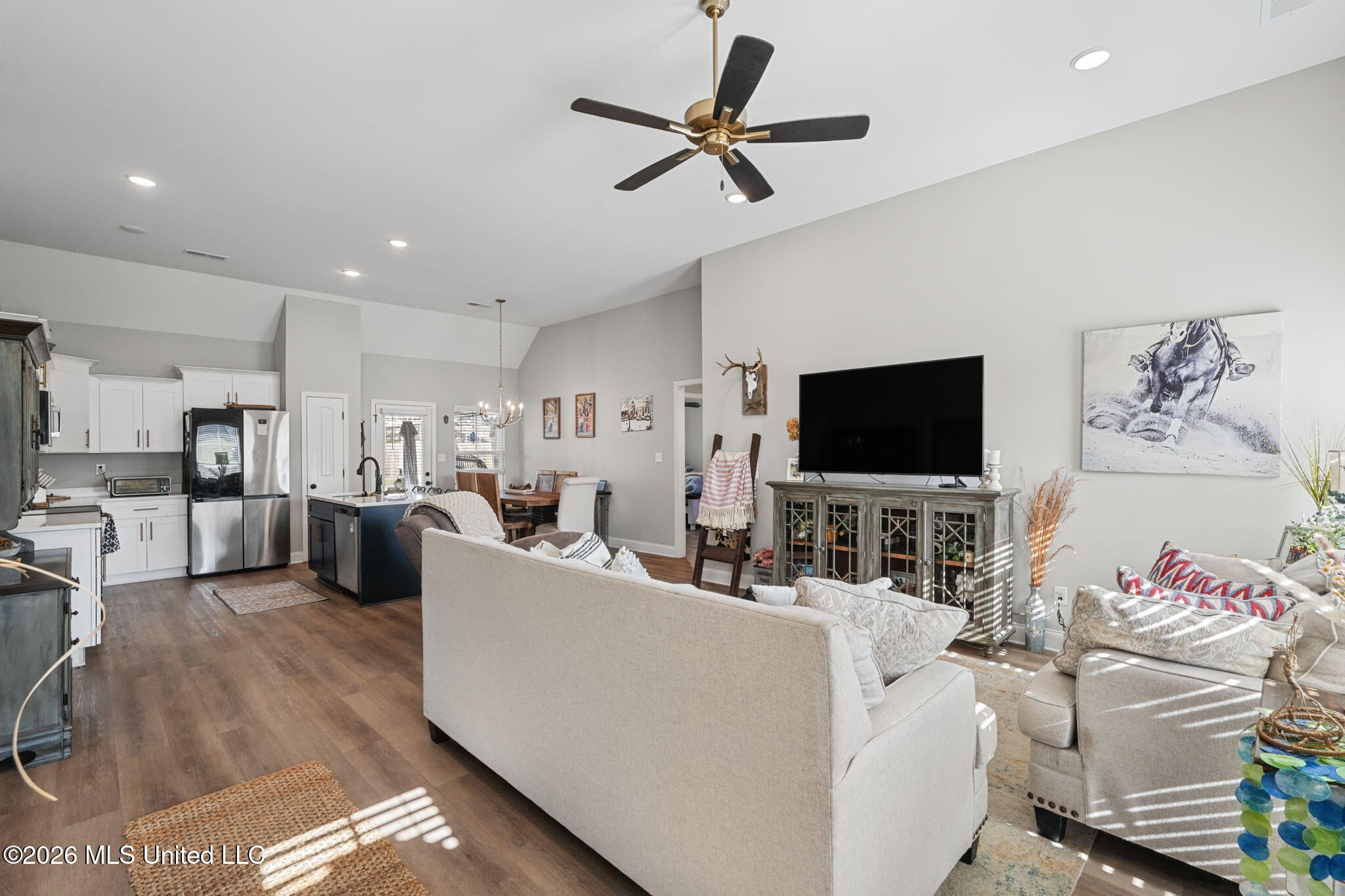 Open-plan living room and kitchen with white sofas, a dark island, and wood floors.