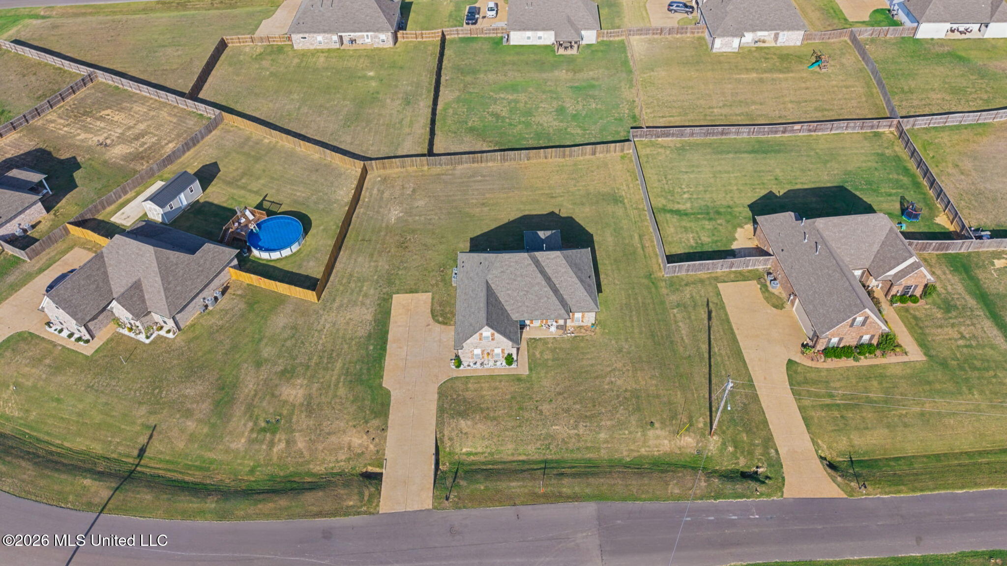 Aerial view of homes with fenced yards and driveways; one yard has an above-ground pool.