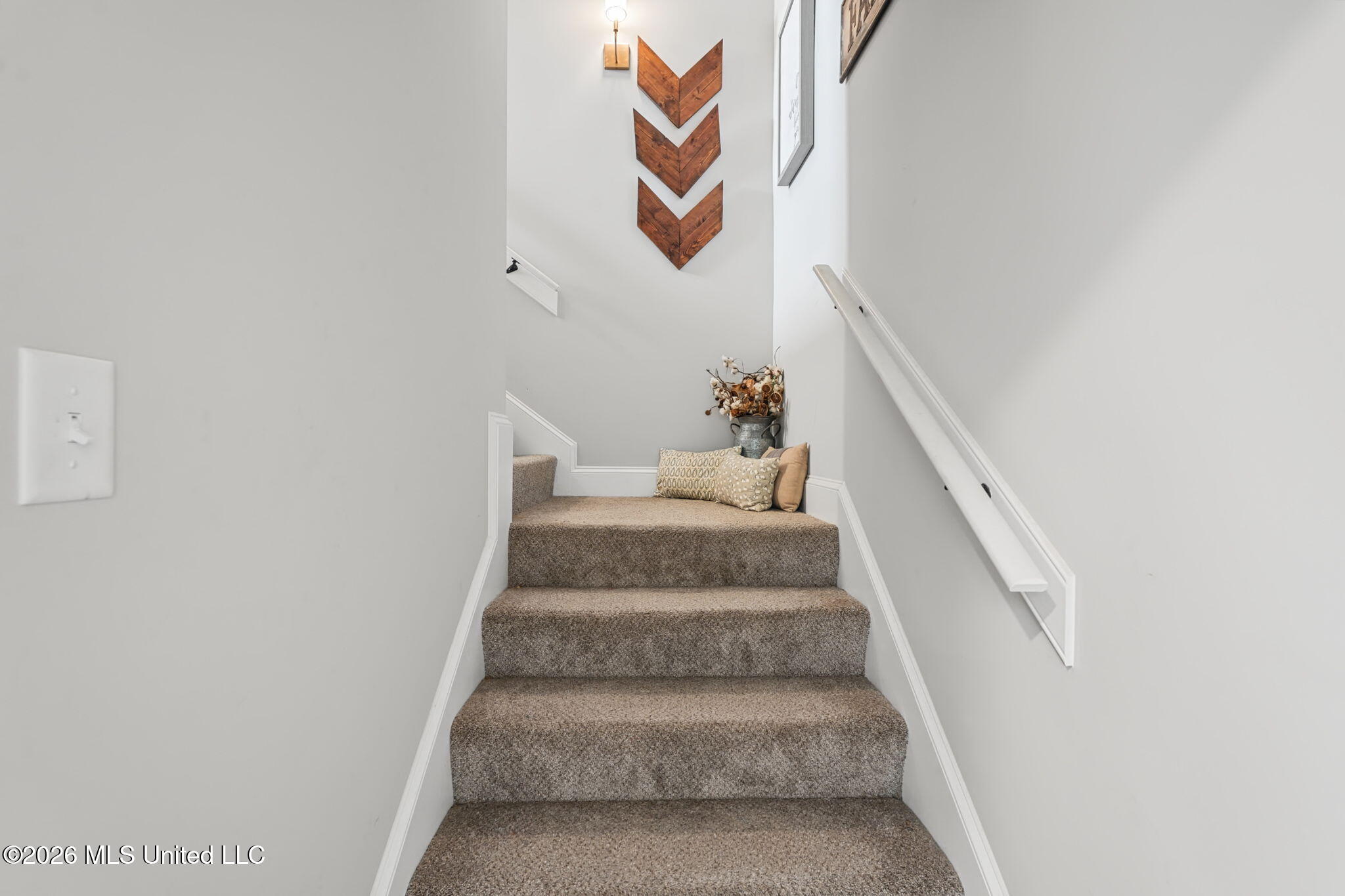 Carpeted staircase with white handrails, a cushioned landing, and wooden chevron wall decor.