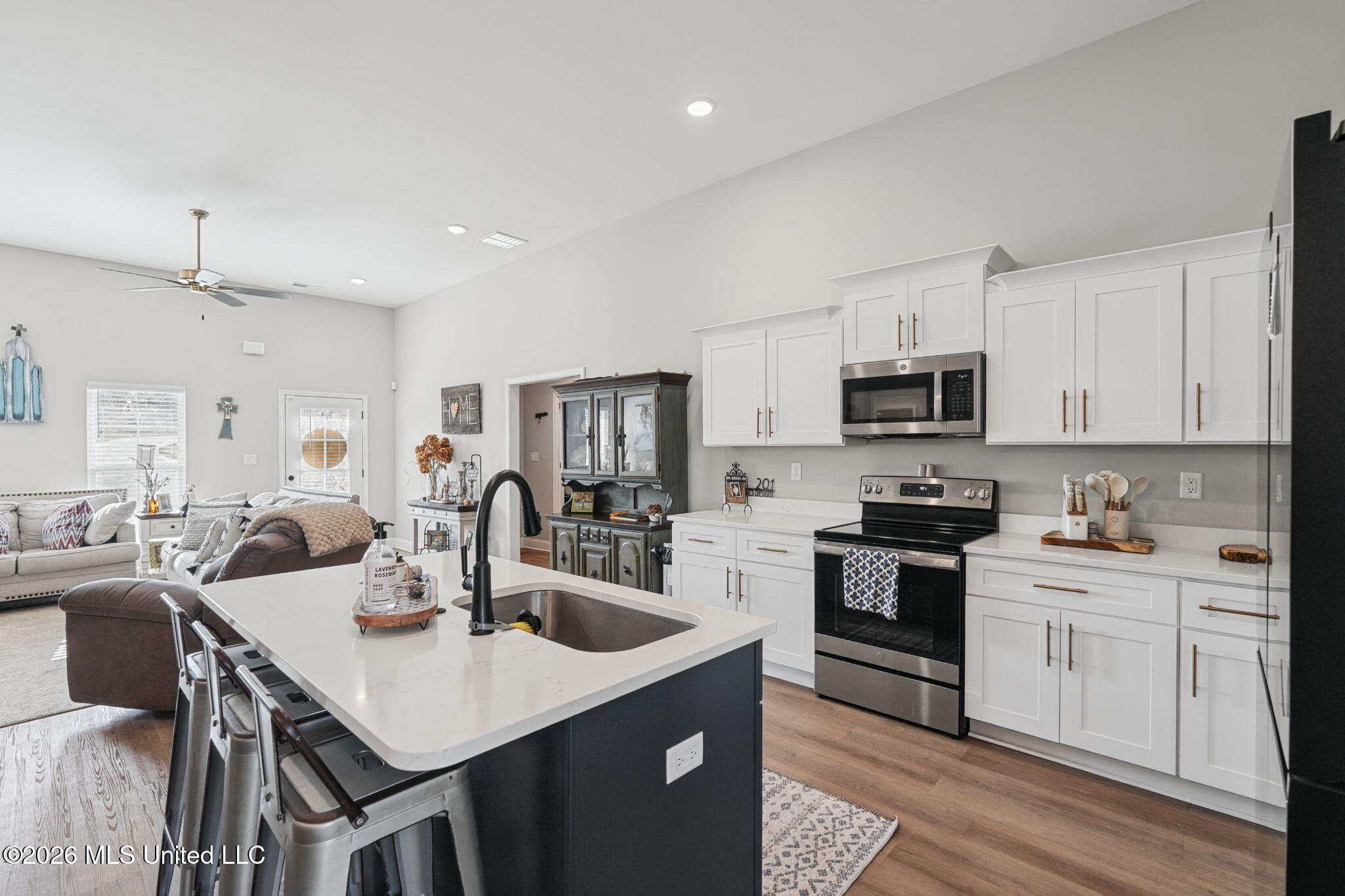 Kitchen with a dark island, white cabinetry, stainless steel appliances, and an adjoining living area.