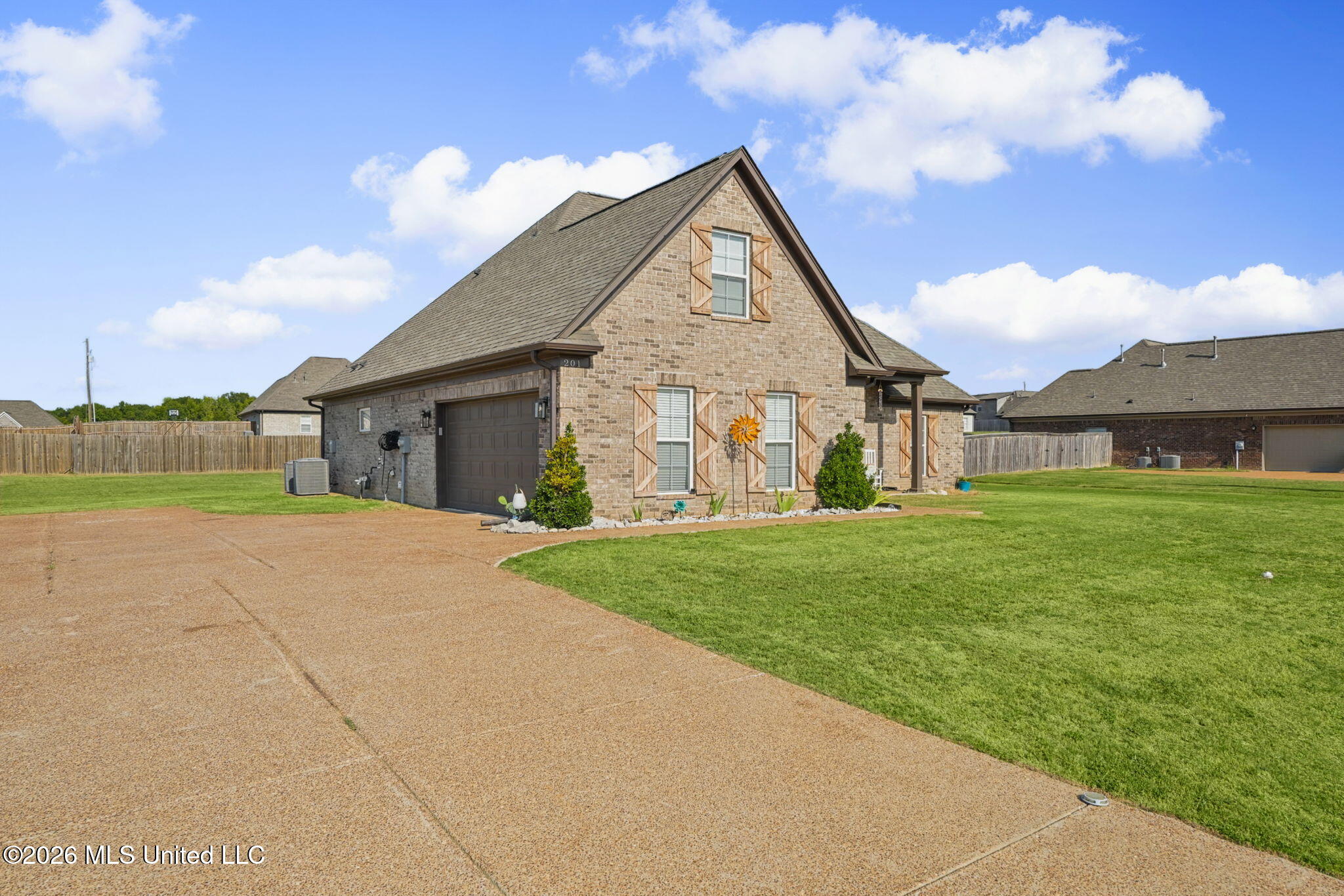 Brick house with steep gabled roof, decorative shutters, attached garage, broad driveway, and green lawn.