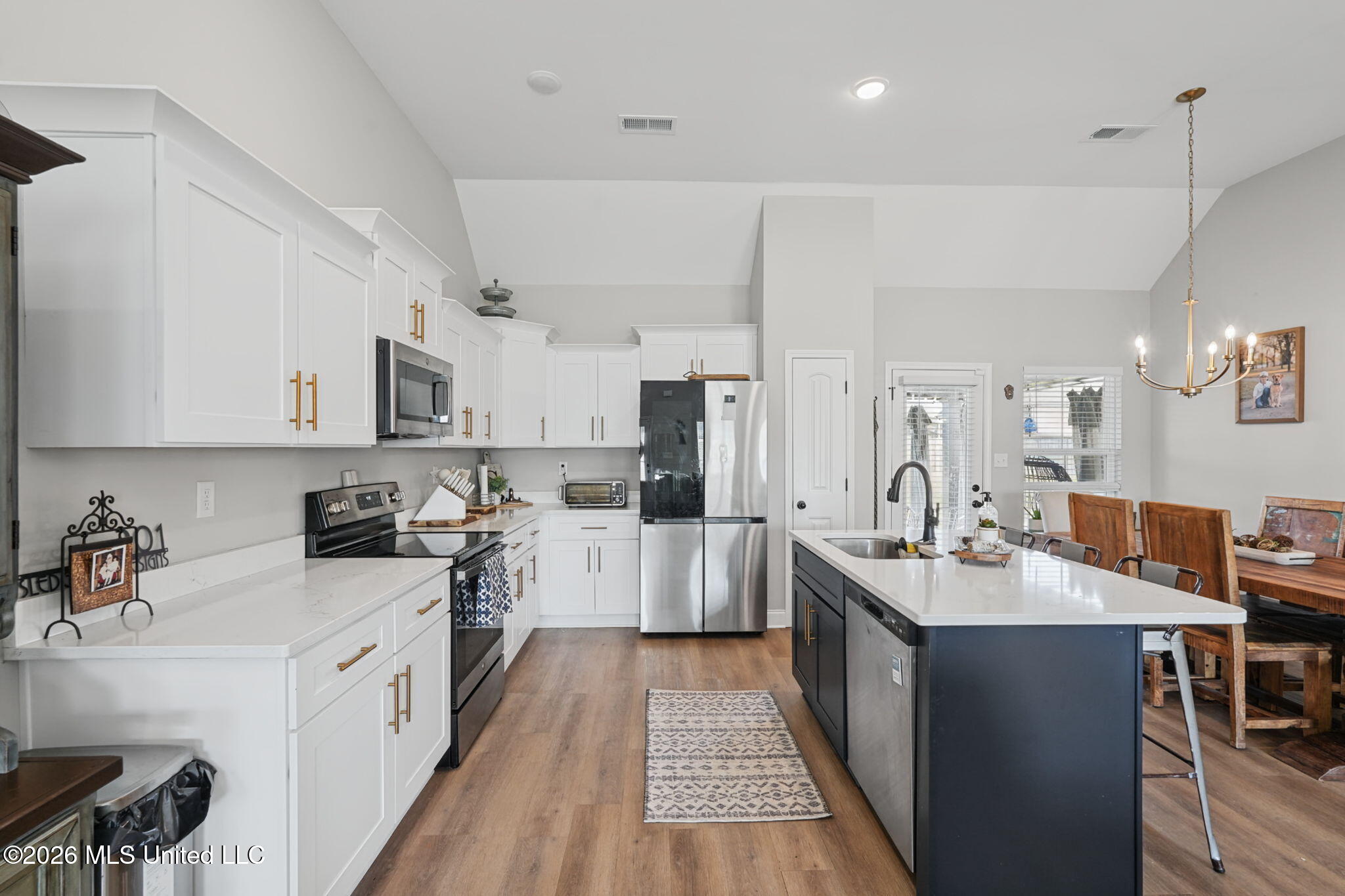 Kitchen with white cabinets, stainless steel appliances, and a dark island beside the dining area.