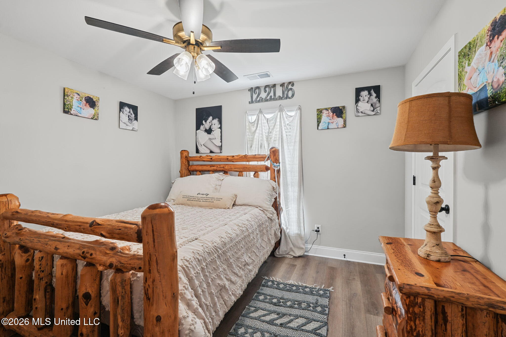 Bedroom with a rustic log bed, cream bedding, and family photos on light gray walls.