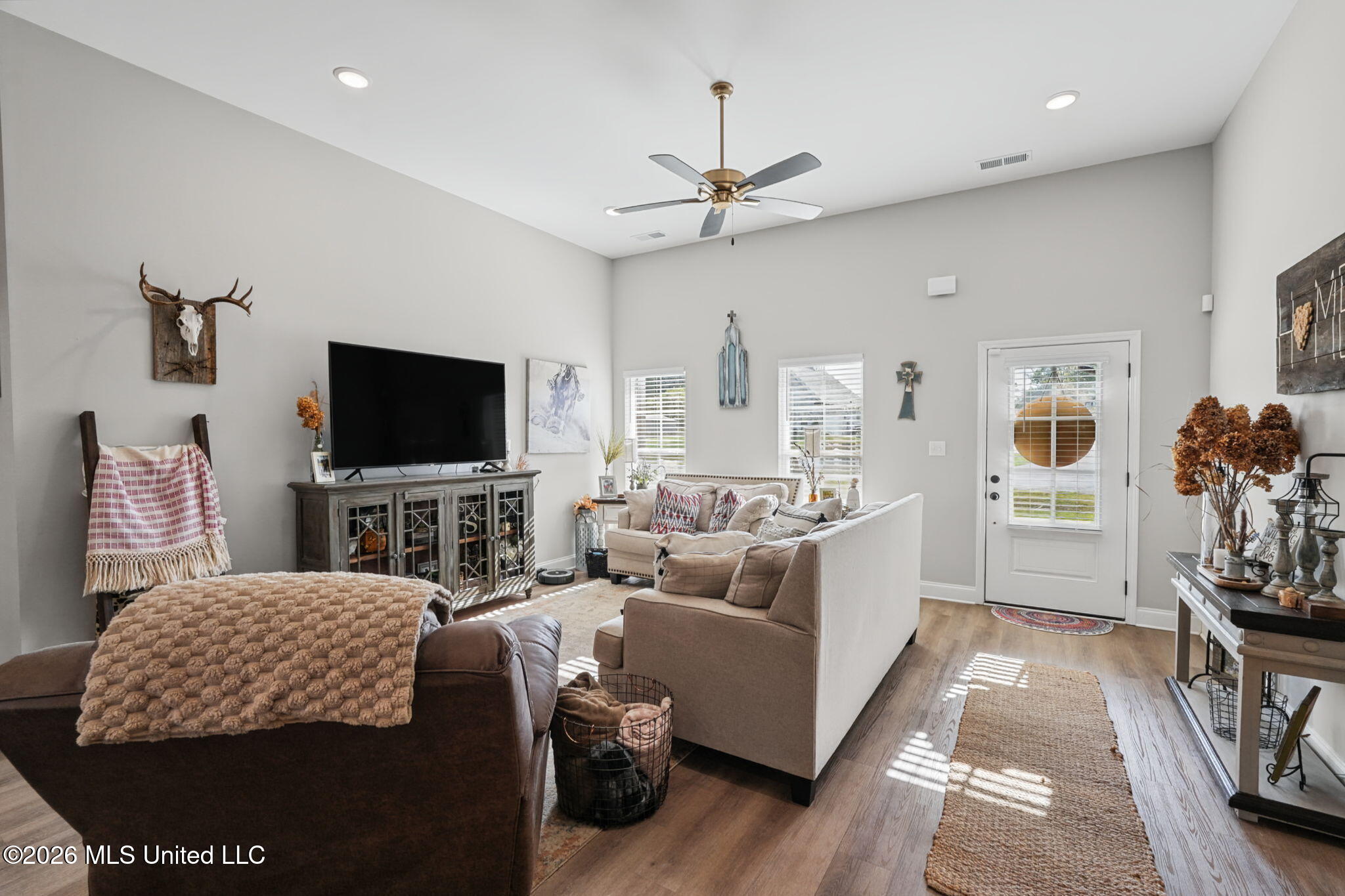 Furnished living room with neutral sofas, a large television, and a glass-paneled front door.
